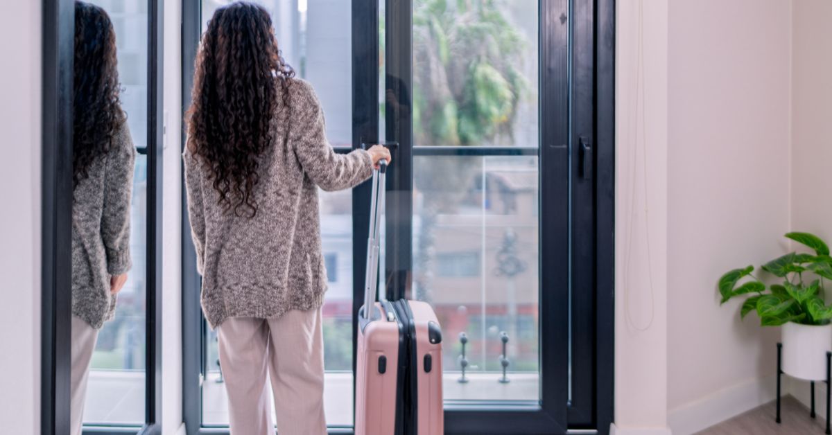 Digital nomad with rolling suitcase opening balcony door in airbnb apartmen