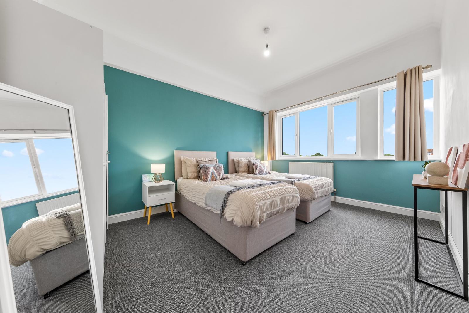 Two beds set against green walls in a bedroom at Twickenham Holiday Let